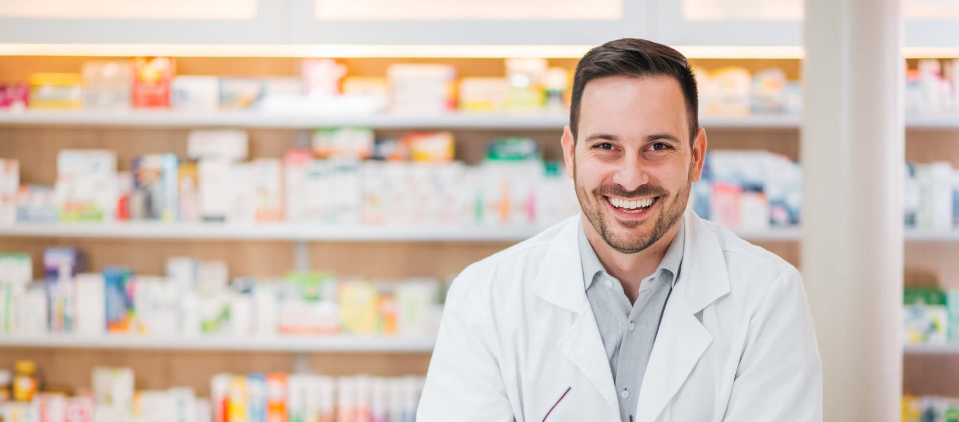 smiling male pharmacist with various types of medicine in the background